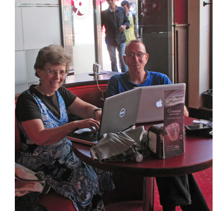 Photo shows Dona and Gene in a booth, each with their laptop open and smiling sheepishly.